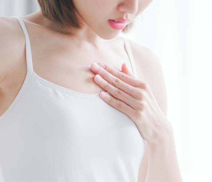 woman wearing white holding breast in pain