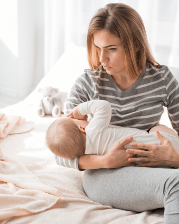 mom looking sad while breastfeeding baby while sitting on bed