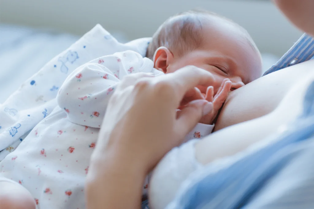 newborn nursing and holding mother's hand