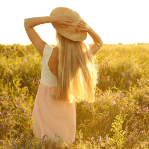 blond woman putting her hands behind her head wearing hat and standing in a field
