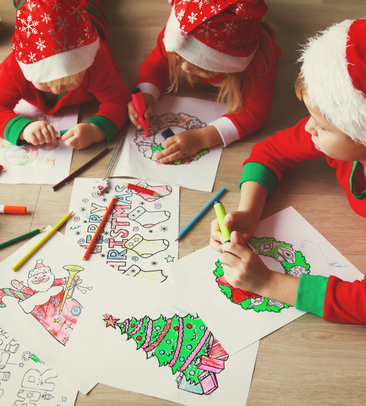 three kids wearing red Christmas pj's and Santa hats doing an easy toddler Christmas activity of colouring Christmas pages together on the floor