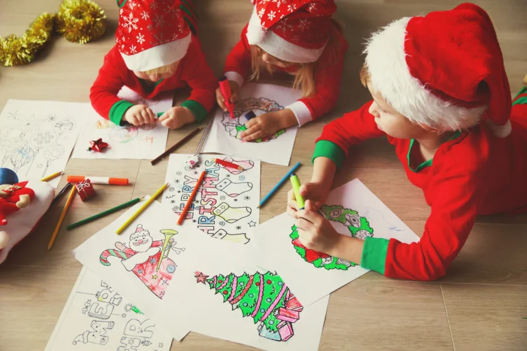 three kids wearing red Christmas pj's and Santa hats doing an easy toddler Christmas activity of colouring Christmas pages together on the floor
