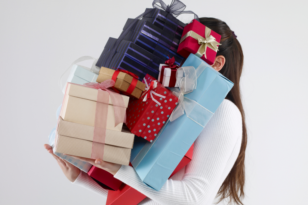 burnet woman wearing white sweater carrying gifts piled so high that they cover her face
