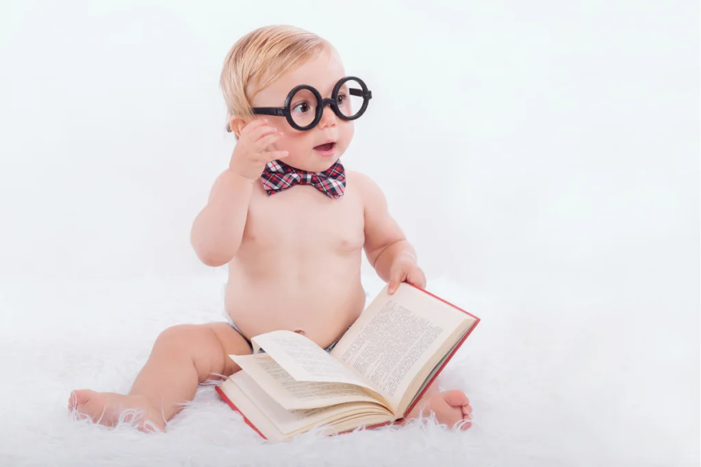 blond shirtless baby boy with bow tie and big black glasses sitting and holding a not a picture book