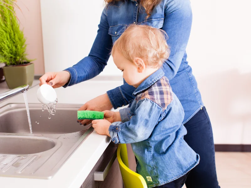 toddler and adult washing dishes at the kitchen sink