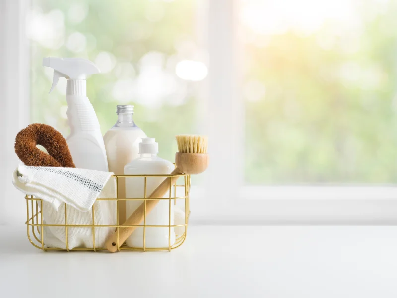 gold metal basket with cleaning supplies sitting in front of a window