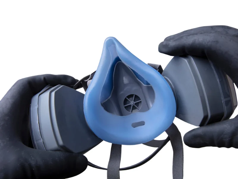 black gloved hands holding a blue and grey respirator with industrial cartridges
