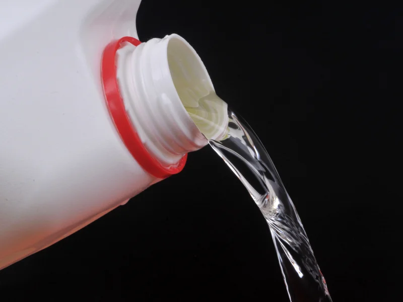 clear liquid pouring out of white plastic bottle with red rim and black background