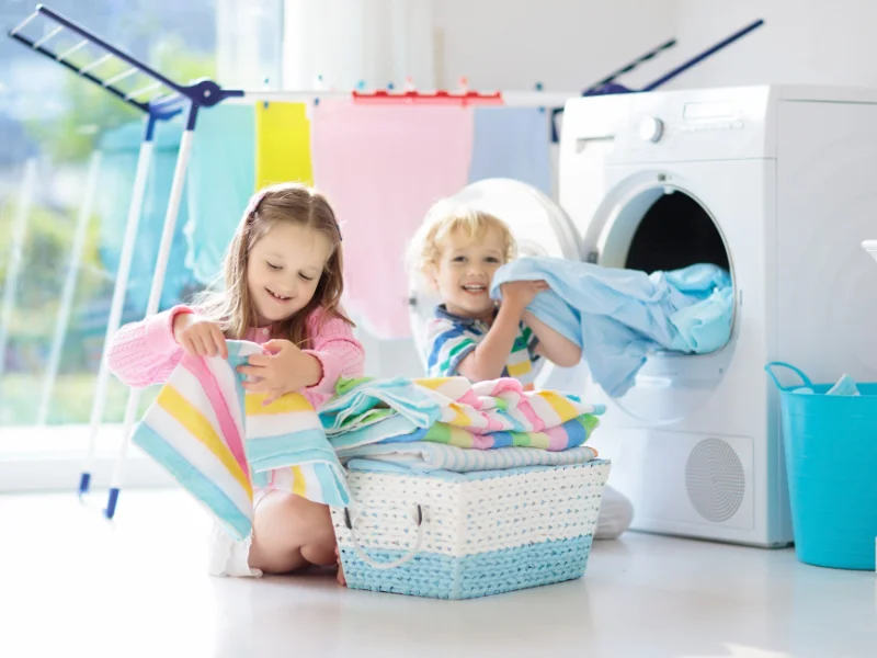 young children smiling helping take laundry out of dryer