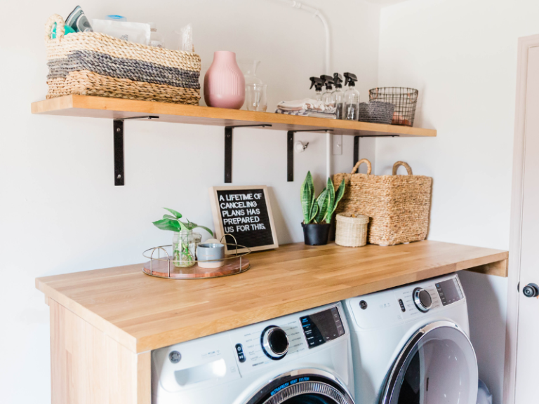 laundry room with butcher block folding table, plants, baskets. Shelf above with natural looking products in it.