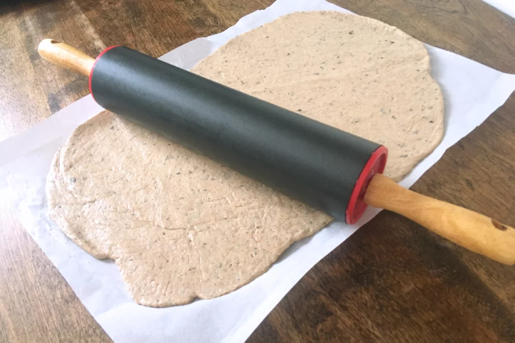 rolling pin on top of sourdough crackers on top of parchment paper