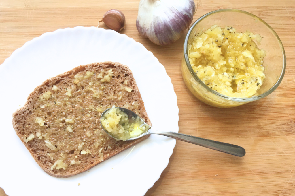 fresh raw garlic olive oil spread on top of spelt sourdough toast with spoon sitting on bread