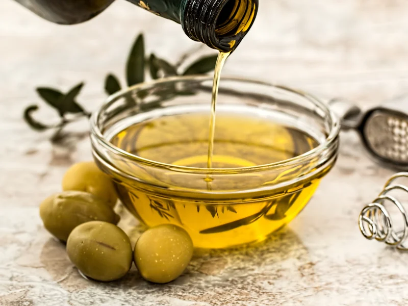 olive oil being poured into a bowl with fresh olives next to it