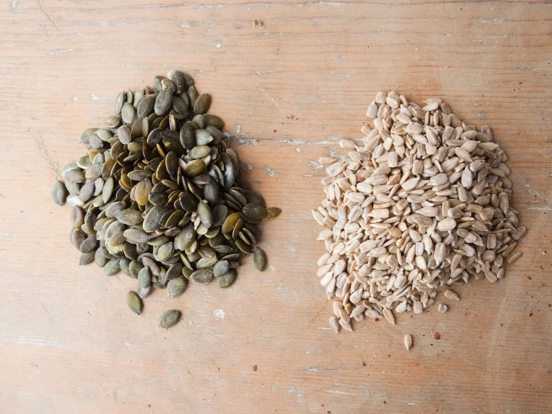 sunflower seeds and pumpkin seeds in a pile on a wooden surface