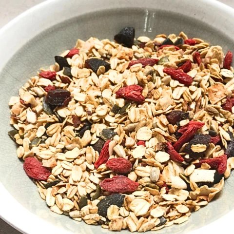 Close up of granola in a bowl with a spoon with goji berries, pumpkins seeds, sunflower seeds, and almonds.