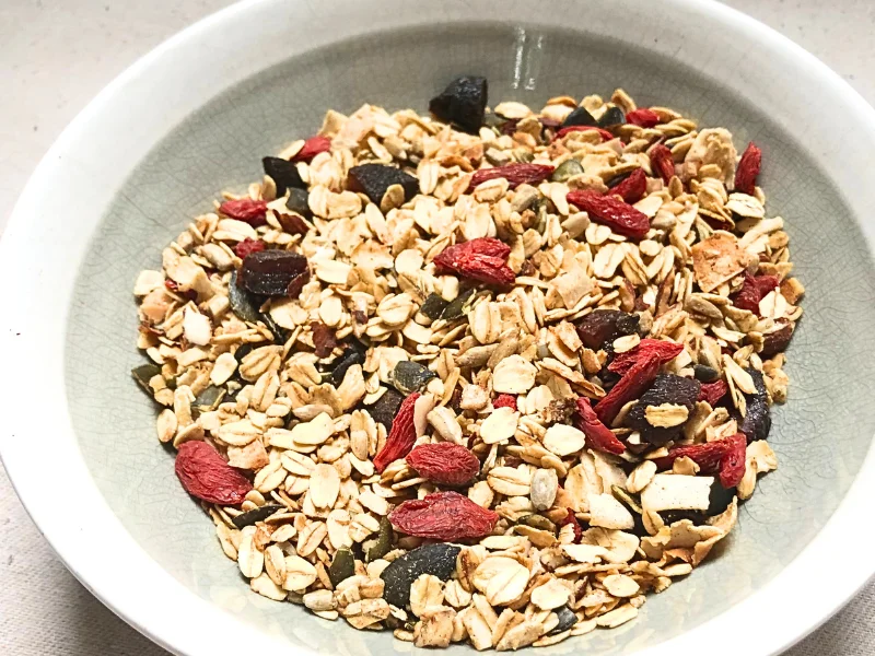 Close up of granola in a bowl with a spoon with goji berries, pumpkins seeds, sunflower seeds, and almonds.