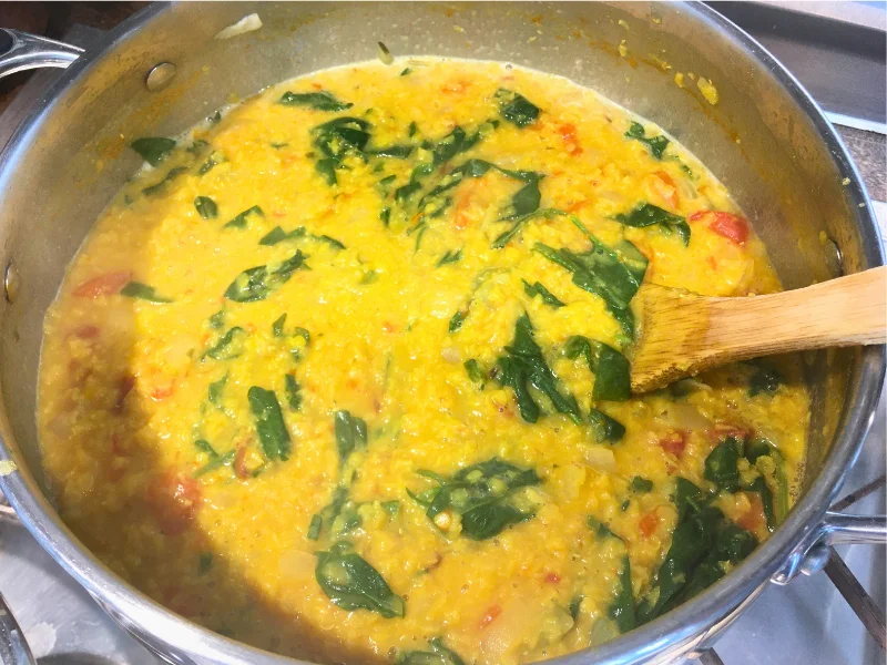 red lentil curry with greens in a pot on the stove