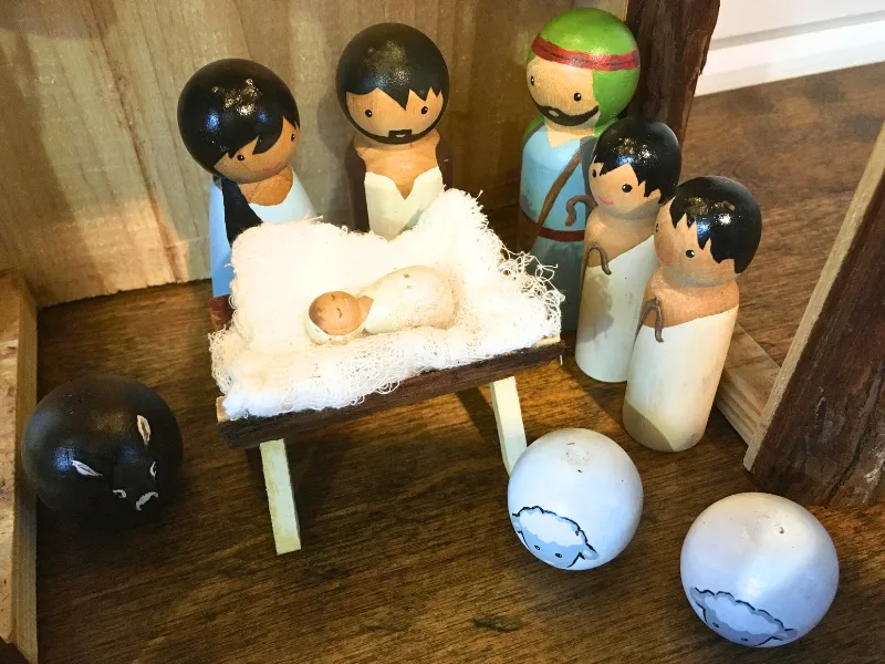 Painted wooden peg nativity scene with Marry, Joseph, Baby Jesus, donkey, sheep, and shepherds in a stable.