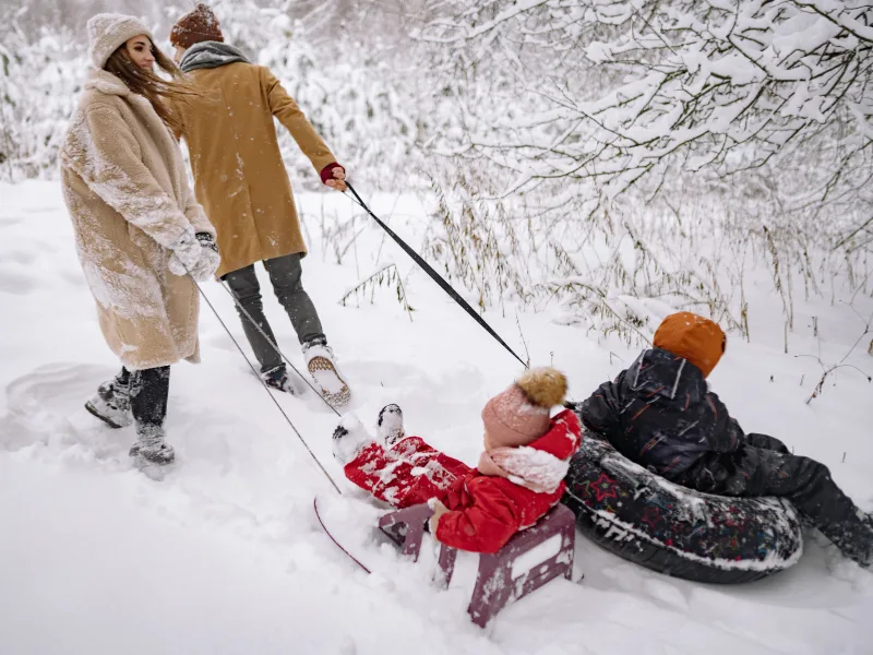 family all bundled up in a snowy woods, parents pulling small children on sleds