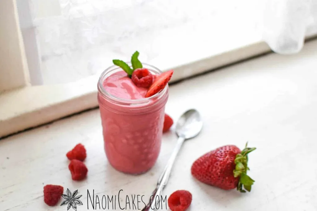 strawberry and raspberry smoothie in a mason pint jar with a spoon next to it near a window