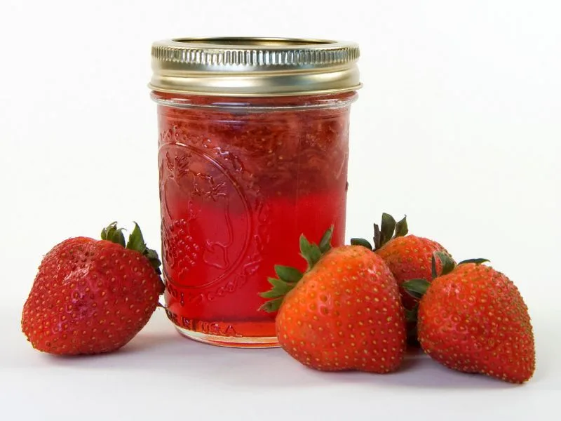 strawberry jam in a pint mason jar with fresh strawberries beside it on a white counter