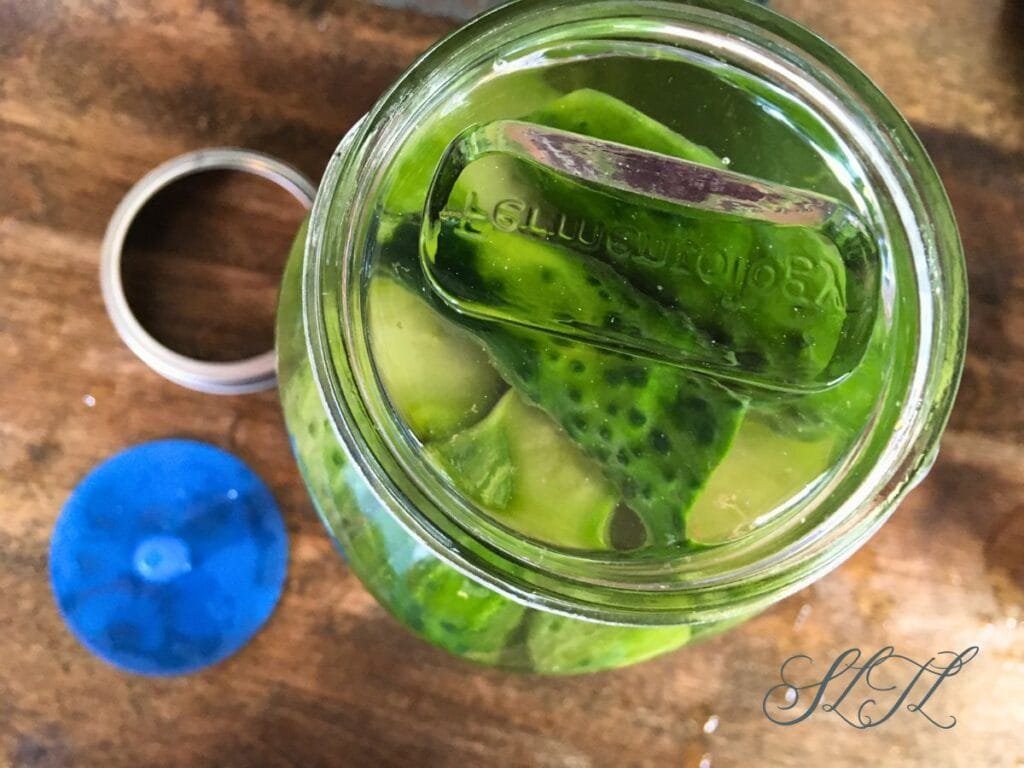 quart jar packed with cucumbers in salt brine with glass weight on top and airlock fermenting lid and jar ring sitting on the counter beside.