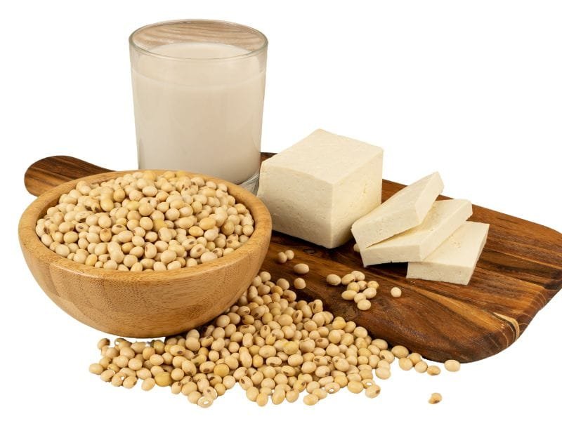 soy beans, soy milk in glass, and tofu on a wooden cutting board