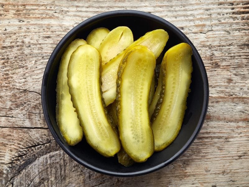 top view of black bowl with sliced pickles on a wooden table.