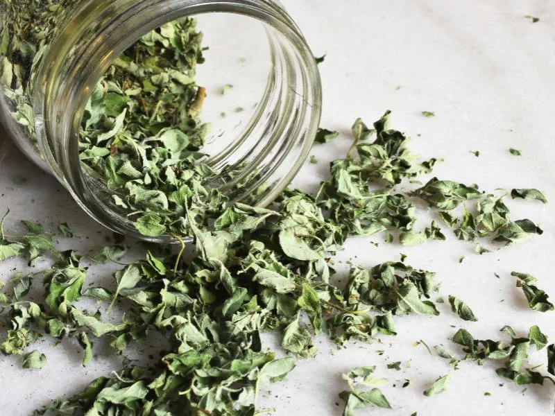 dried oregano spilling out of a mason jar onto a white table