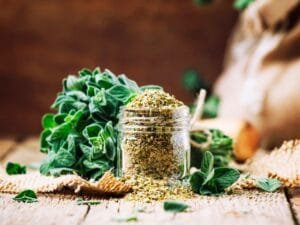 fresh bundle of oregano with a jar of dried oregano spilling over sitting on a wooden table