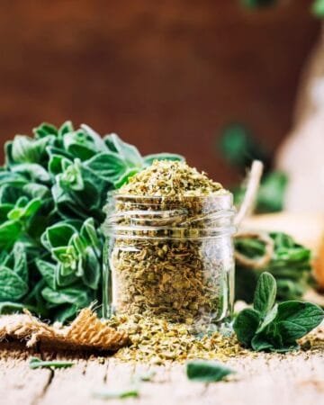 fresh bundle of oregano with a jar of dried oregano spilling over sitting on a wooden table