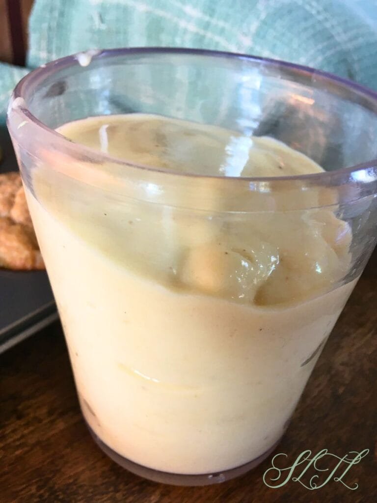 Close up of pinna colada smoothie in clear cup with teal tea towel in background on wooden counter.