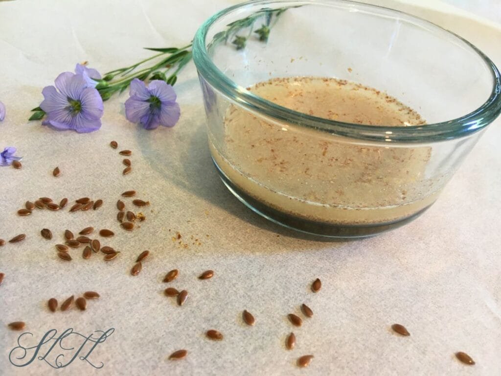 flaxseed and flaxseed flower sitting next to glass bowl of flax seed egg
