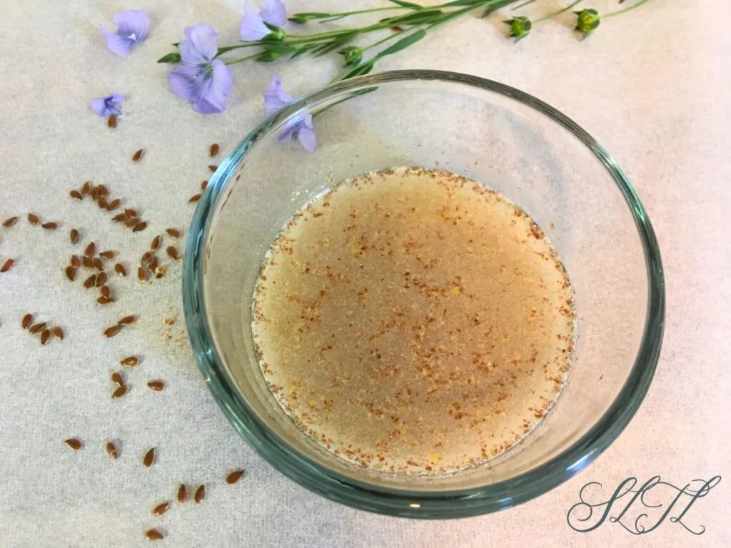 flaxseed and flaxseed flower sitting next to glass bowl of ground flax seed egg