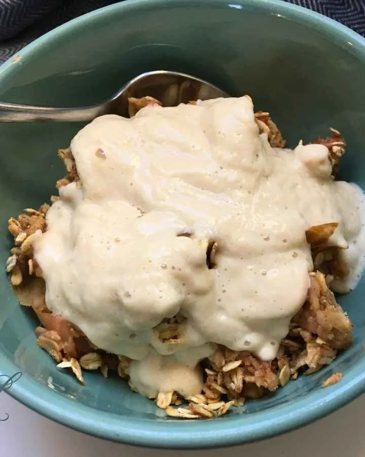 vegan apple rhubarb crisp topped with pear cream in a teal bowl with a spoon