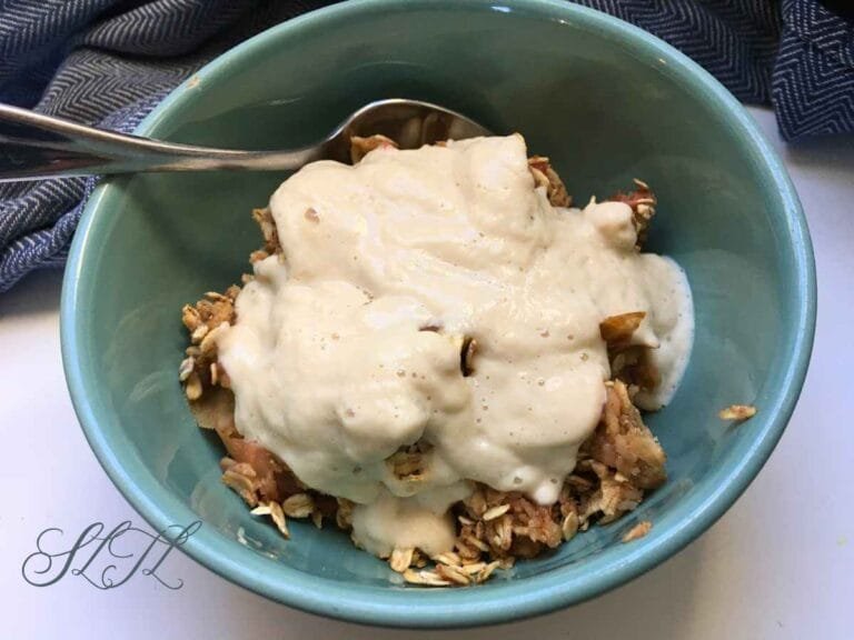vegan apple rhubarb crisp topped with pear cream in a teal bowl with a spoon