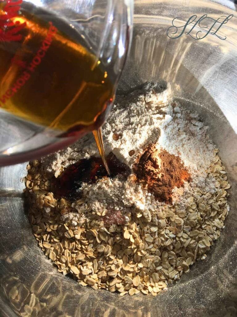 in a mixing bowl oats, spet flour, cinnamon, salt, maple syrup being poured in