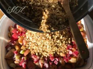 vegan apple rhubarb crisp crumble being poured on top of chopped apples and rhubarb sprinkled with cinnamon and spelt flour