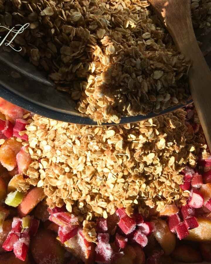 vegan apple rhubarb crisp crumble being poured on top of chopped apples and rhubarb sprinkled with cinnamon and spelt flour