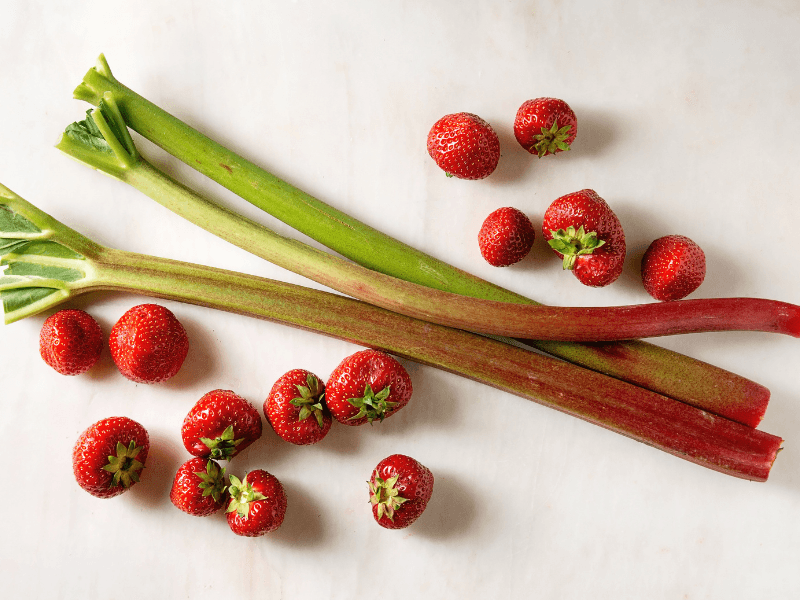 Rhubarb stocks and strawberries on white countertop.