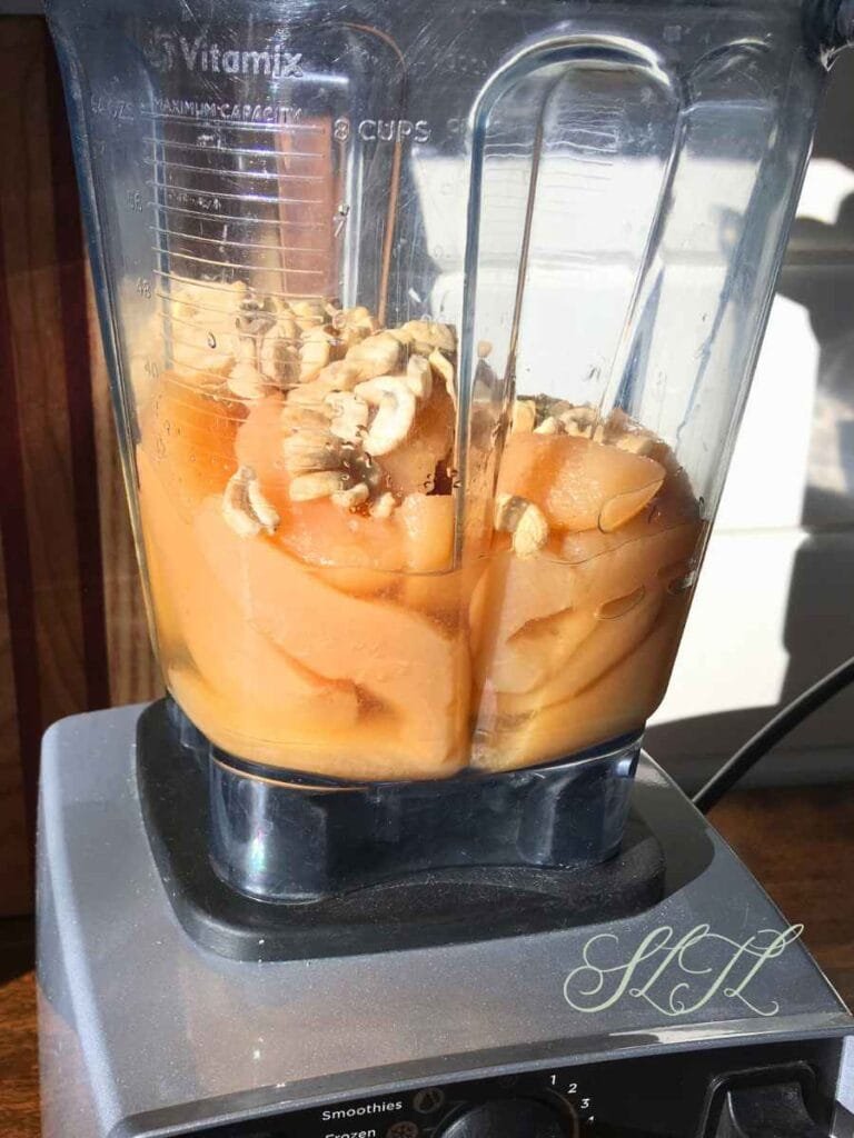 Side view of a Vitamix with canned pears, raw cashews, salt and vanilla extract in blender.